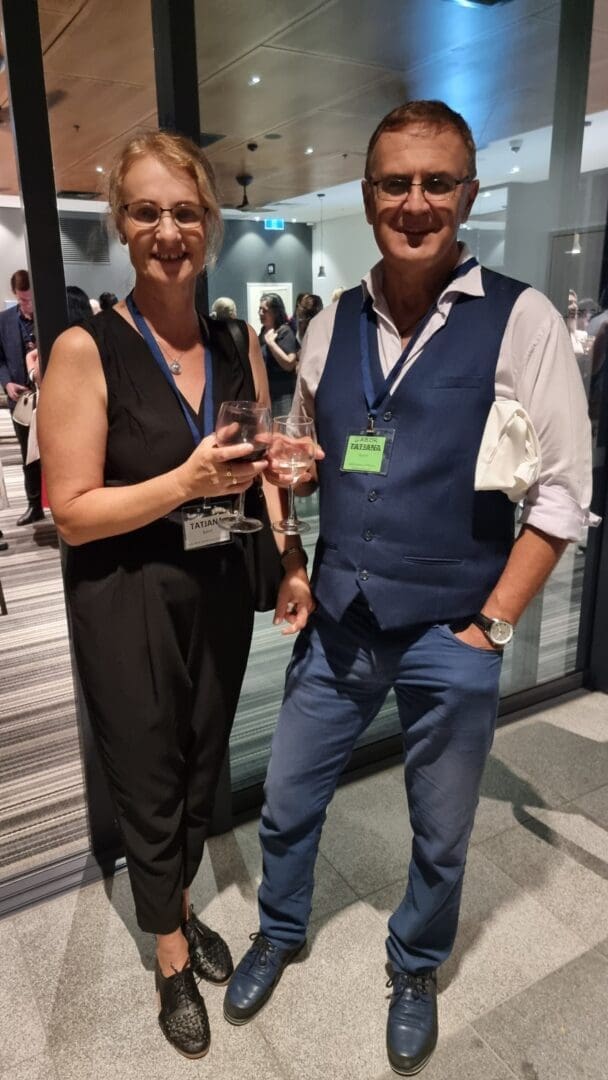 Man and woman casually dressed vests cocktails smiling posing for camera OUM reception