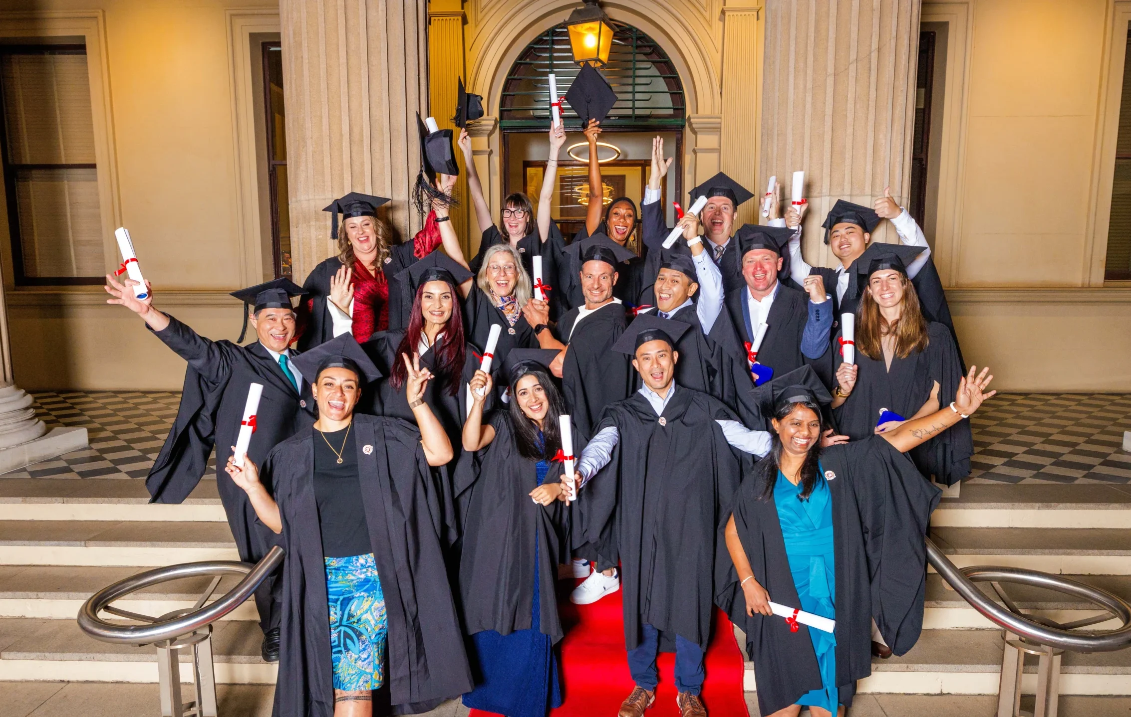 Excited OUM graduates in caps and gowns holding diplomas and celebrating together on a staircase during OUM's 2025 graduation ceremony
