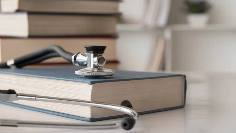 Stethoscope resting on top of a closed medical textbook, with more stacked books in the background, symbolizing medical education and study