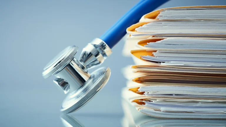 Close-up of a stethoscope resting against a tall stack of paper folders and documents, symbolizing medical records, research, or academic studies in healthcare