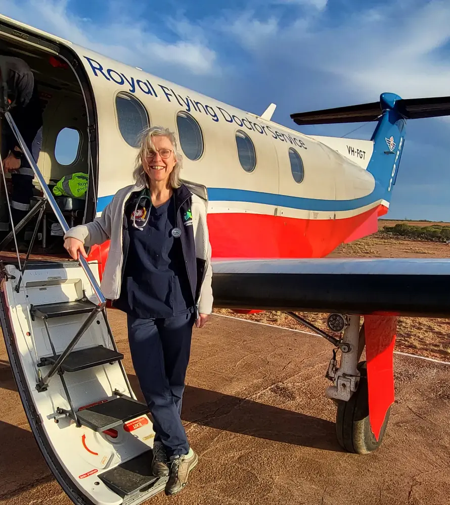 a woman dressed in blue scrubs boarding a small jet plane