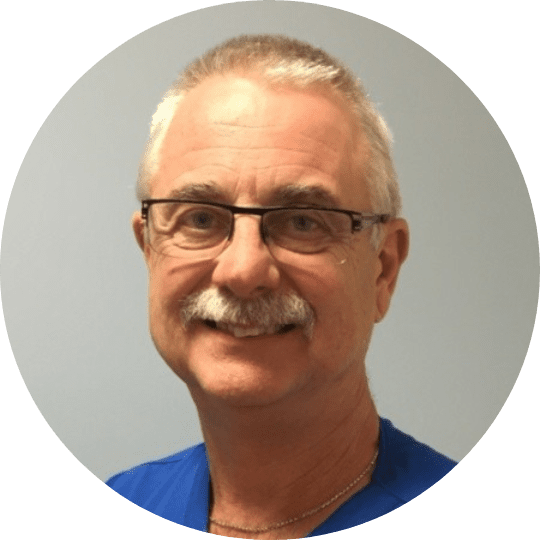 headshot of older male doctor with gray hair, glasses, mustache, and smiling wearing blue scrubs