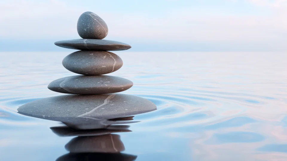 A stack of smooth, gray stones balanced on top of each other, reflected in calm water.