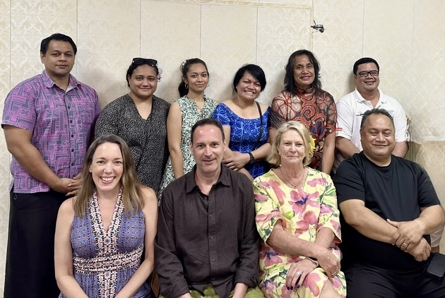 A group of ten people, colleagues, are gathered together. They are all smiling and appear to be posing for a photo. The group is diverse. Some wearing business casual attire, while others have more casual clothing.
