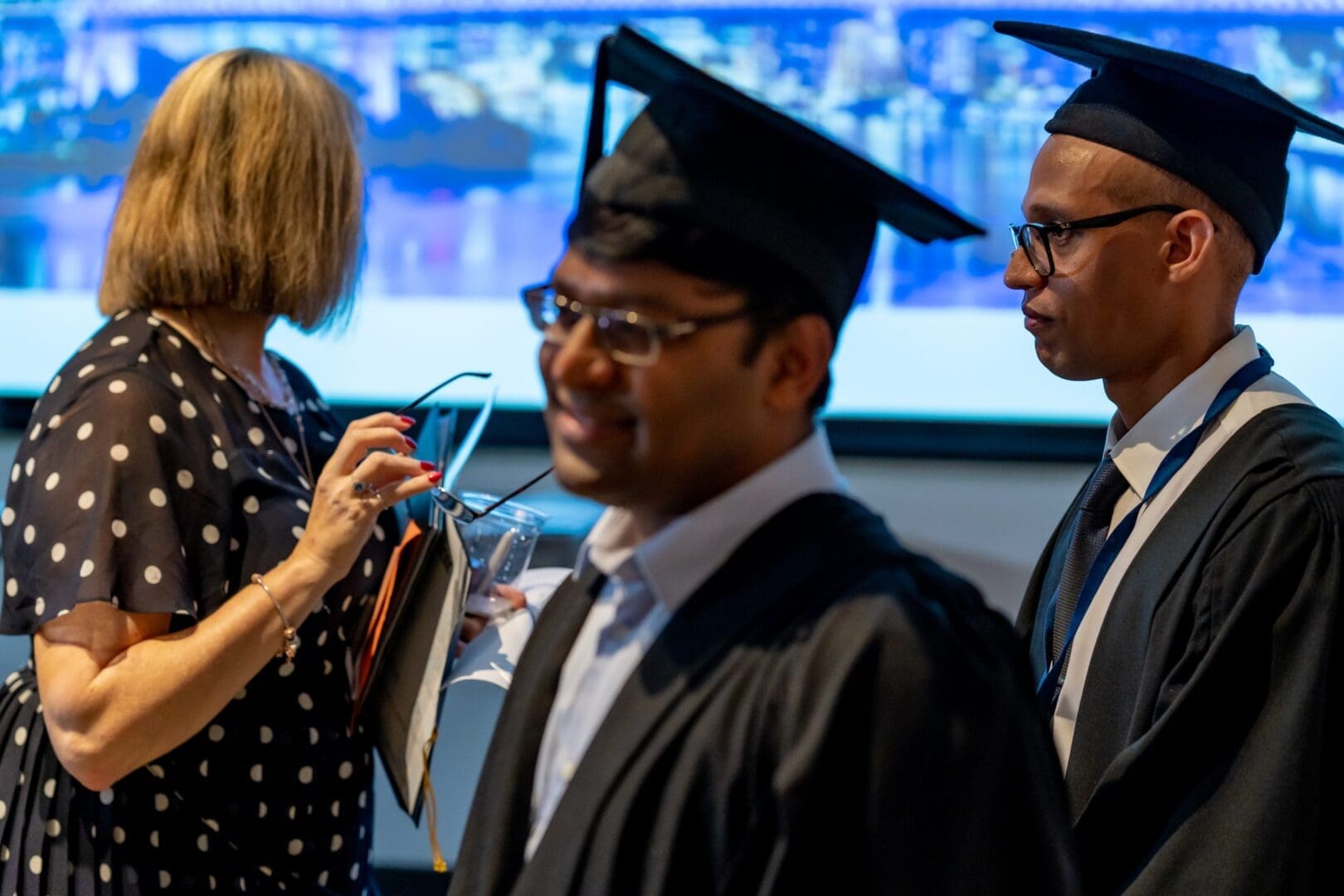 Three people woman on left polka dot dress two dark skin men graduating mortar boards OUM