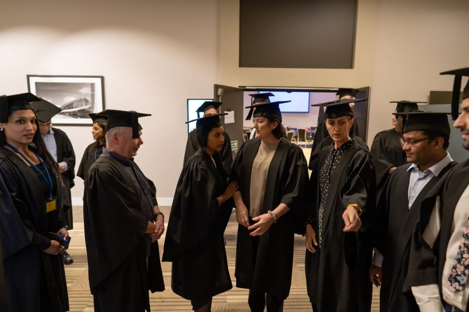 Dozen men and women in caps and gowns assembling for med school graduation OUM