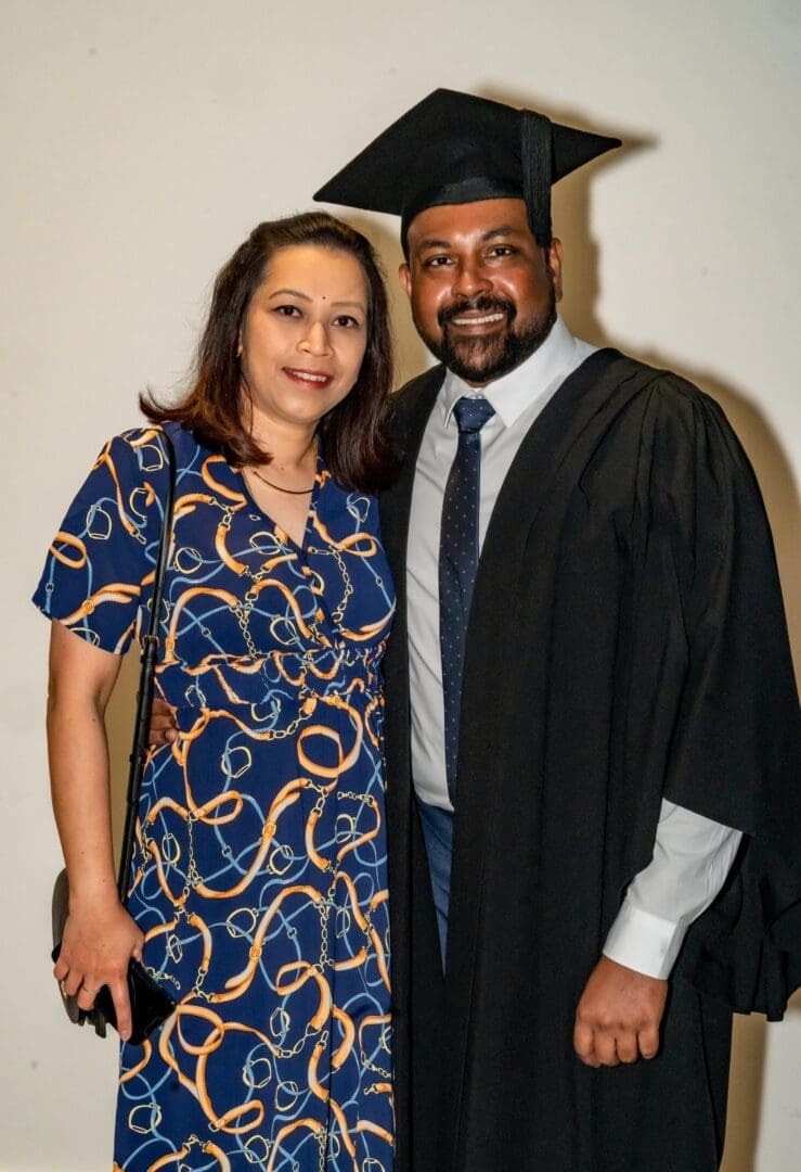 Woman shoulder length dark hair blue gold dress brown skin man beard black cap gown smiling OUM