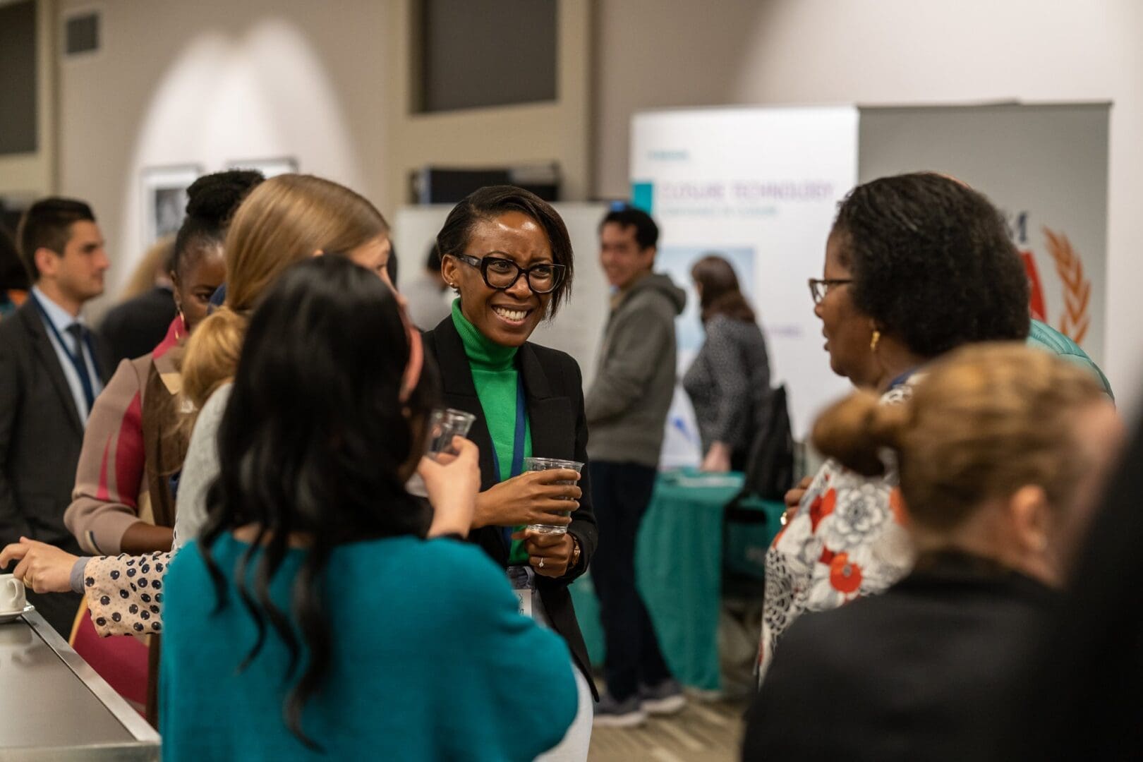 Four professional women in circle chatting at med conference one in green shirt laughing OUM