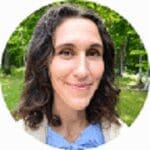 headshot of smiling female physician with long brown hair wearing white jacket outdoors