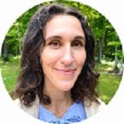 headshot of smiling female physician with long brown hair wearing white jacket outdoors