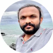 Portrait of a man wearing a light gray polo shirt with a full black beard. Ocean in the background.