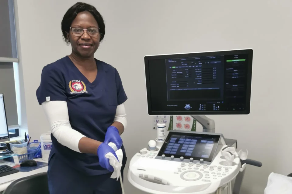 Black female doctor smiling wearing blue scrubs next to a health monitor station