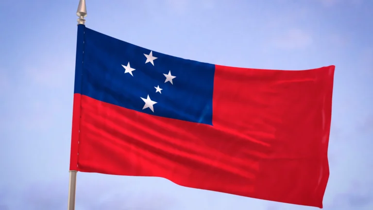 National flag of Samoa waving on a flagpole, featuring a red field with a blue rectangle in the upper left corner containing five white stars