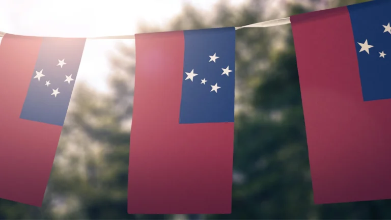String of Samoan flags hanging outdoors, featuring a red background with a blue rectangle in the top left corner displaying the Southern Cross constellation