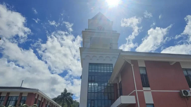 Red and white building with a clock tower and large glass windows, photographed under a bright sunny sky with scattered clouds