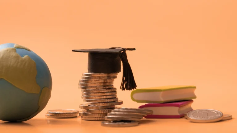 Stack of coins topped with a graduation cap beside miniature books and a globe, symbolizing education costs, scholarships, and global learning opportunities