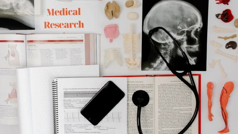 Medical research study setup with anatomy models, textbooks, an X-ray of a skull, a stethoscope, and notes arranged on a desk