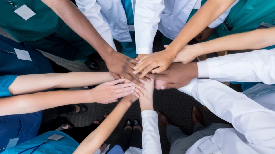 Diverse group of healthcare professionals and medical students in scrubs and white coats stacking hands together in teamwork and unity