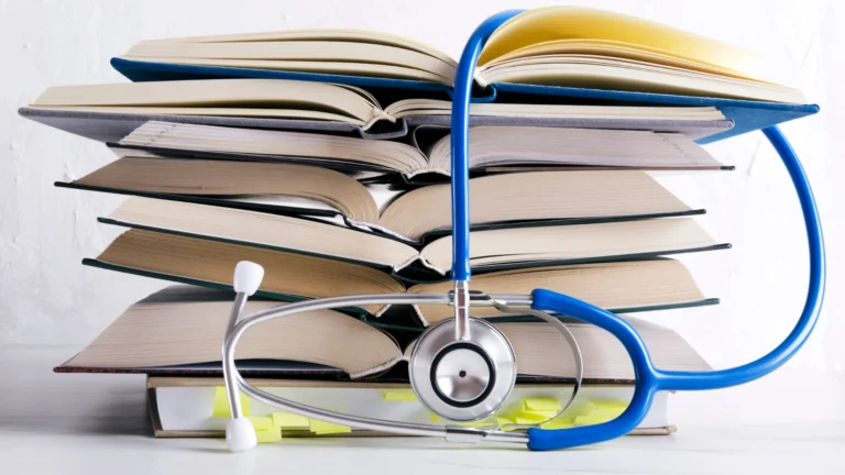 Stack of open medical textbooks with a blue stethoscope draped over them and sticky notes visible at the bottom
