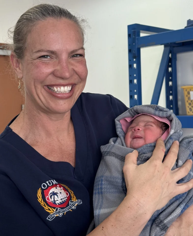 A smiling woman in a scrub top is cradling a newborn baby in her arms.
