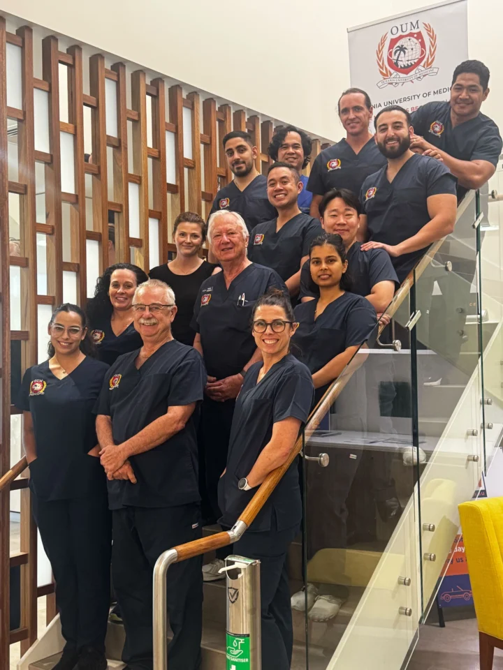 Diverse group of doctors wearing dark blue scrubs standing on staircase smiling for a picture.