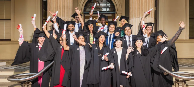 Excited OUM graduates in caps and gowns holding diplomas and celebrating together on a staircase during OUM's graduation ceremony