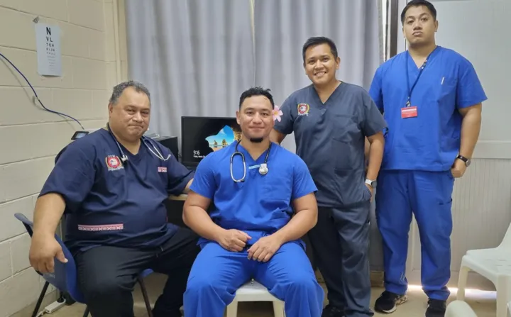 Four medical professionals, two men and two women, are posing for a photo. They are wearing blue scrubs and are smiling and relaxed.