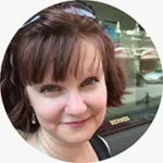 Headshot of woman with brownish reddish short hair with bangs smiling and looking at camera