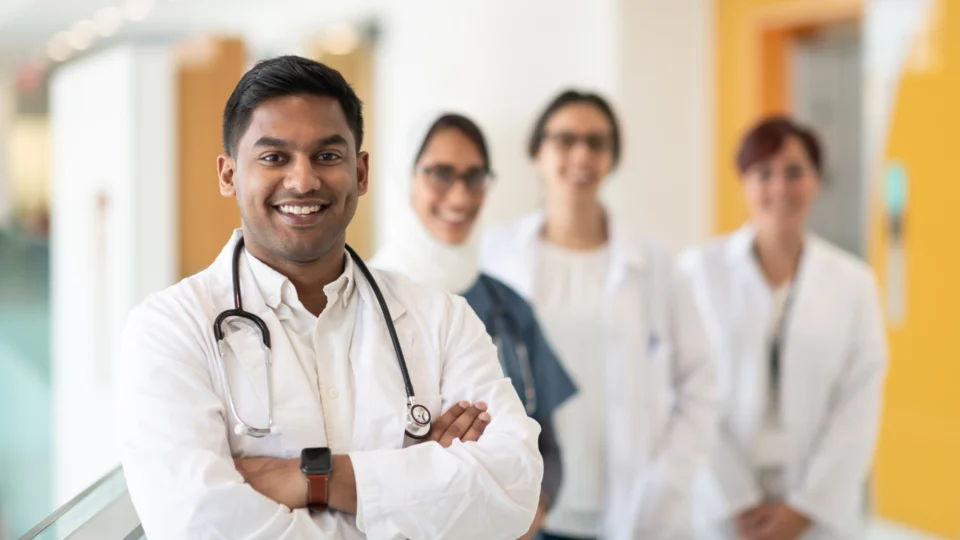 Four male and female doctors wearing white scrubs standing and smiling for a picture