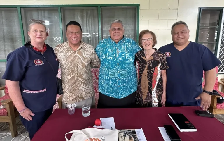 divers group of older adults, two dressed in dark blue scrubs standing around a maroon table.