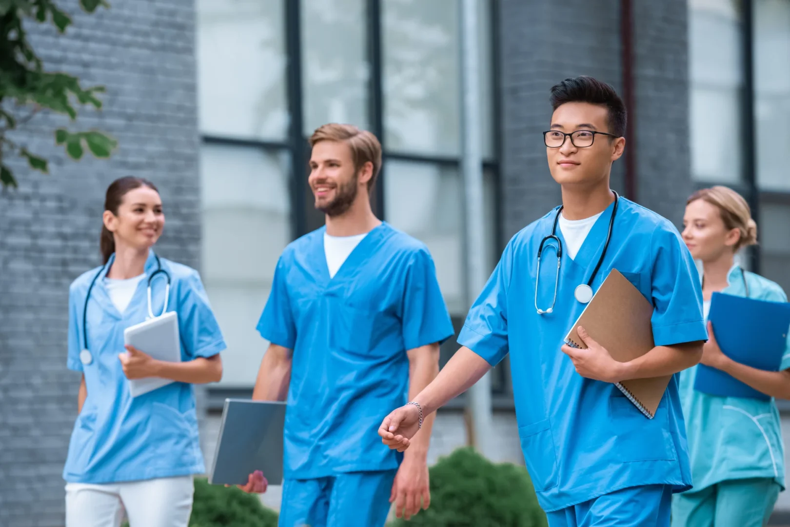 Young male and female doctors walking happily outside in bright blue scrubs