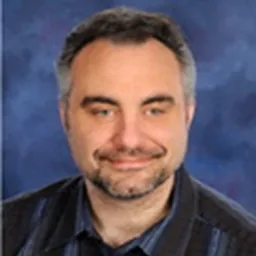headshot of older man wearing a black shirt and smiling against a royal blue background