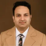 headshot of man wearing a tan suit, white shirt, and dark tie.