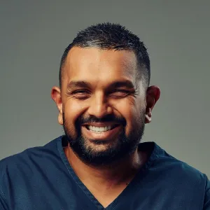 smiling male doctor with short dark hair and beard against a gray gradient background