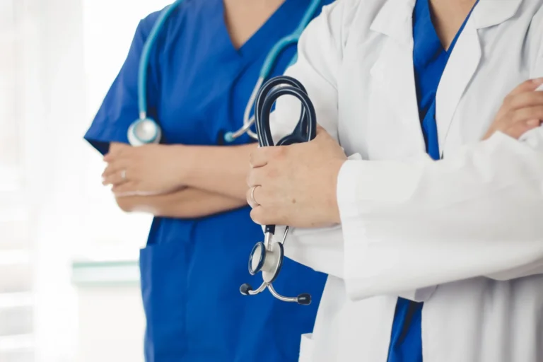 two doctor one wearing white scrubs other wearing blue holding a stethoscope
