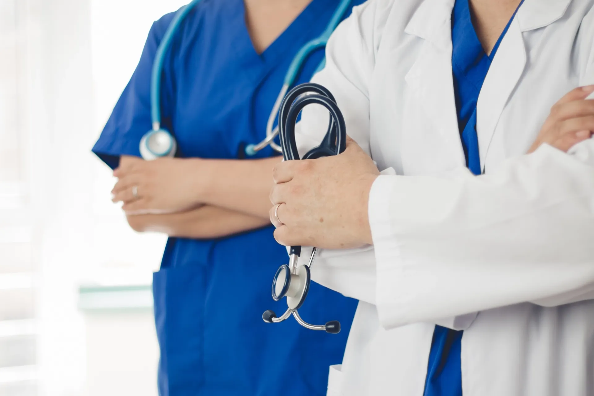 two doctor one wearing white scrubs other wearing blue holding a stethoscope
